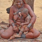 Een vrouw van de Himba stam met haar kind en koopwaar in Otjikandero<br/>Copyright © JTravel.nl Een vrouw van de Himba stam met haar kind en koopwaar in Otjikandero / Copyright © JTravel.nl